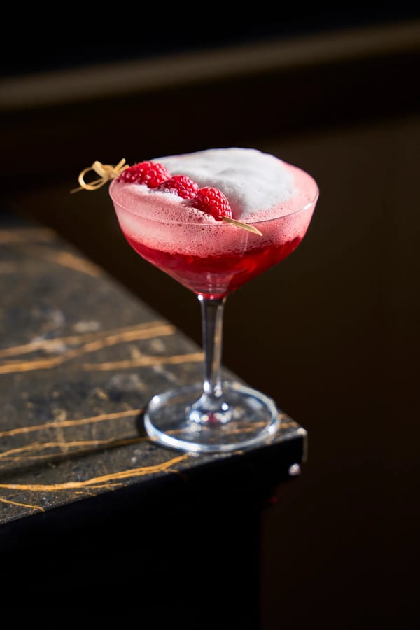 Cocktail ai lamponi con schiuma in coppa martini su bancone di marmo nero, fotografia drink e mixology