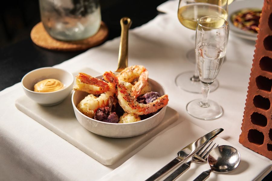 Gamberi grigliati su padellino con salsa, flute di champagne e tovaglia bianca — aperitivo gourmet, fotografo food Potafiori Milano