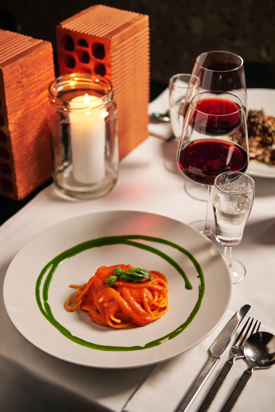 Spaghetti al pomodoro con spirale di pesto e candela accesa, calici di vino rosso — fotografia pasta ristorante Potafiori Milano