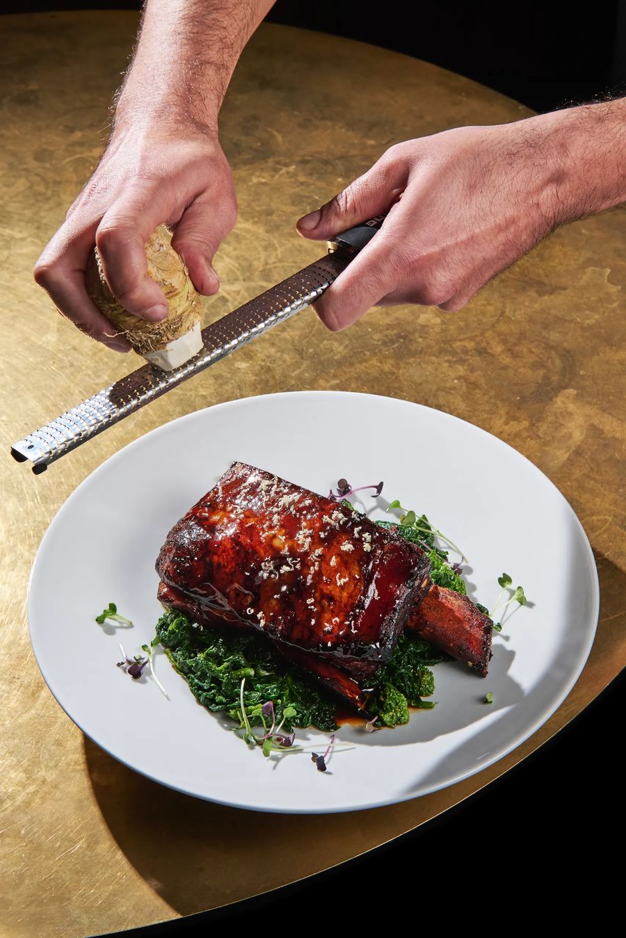 Chef che grattugia formaggio su costolette di manzo caramellate con rapini saltati — azione in cucina gourmet, fotografo Potafiori Milano