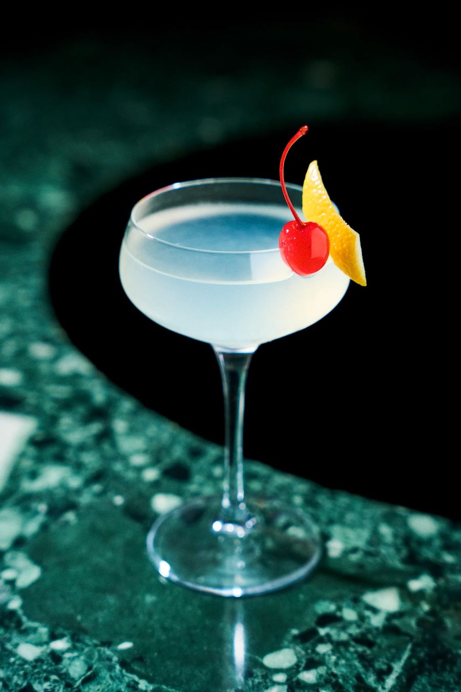 Cocktail bianco con ciliegia maraschino e scorza d'arancia in coppa coupe su marmo verde — drink photography Alchimia Milano