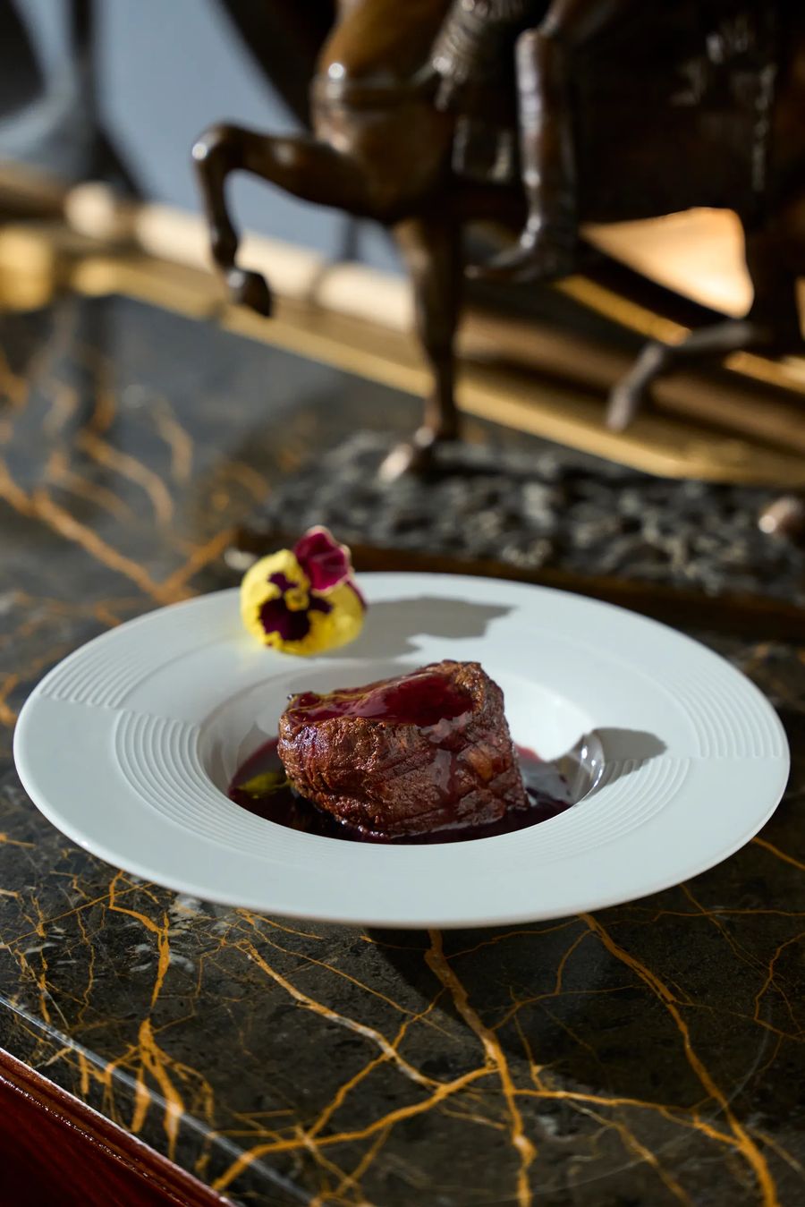 Piccione brasato con riduzione di vino rosso e fiore edule su piano in marmo dorato — piatto gourmet, fotografo food Alchimia Milano