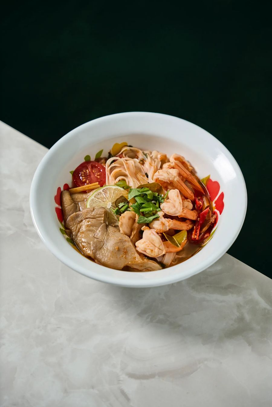 Zuppa di noodles di riso con gamberetti e maiale in ciotola floreale su marmo bianco — cucina thai autentica, fotografo food Milano