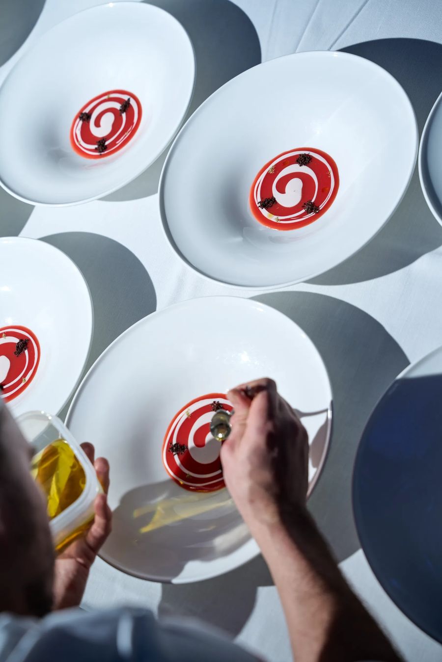 Vista dall'alto di cinque piatti con spirale di salsa rossa impattati durante il servizio — backstage haute cuisine, fotografo food professionale Milano