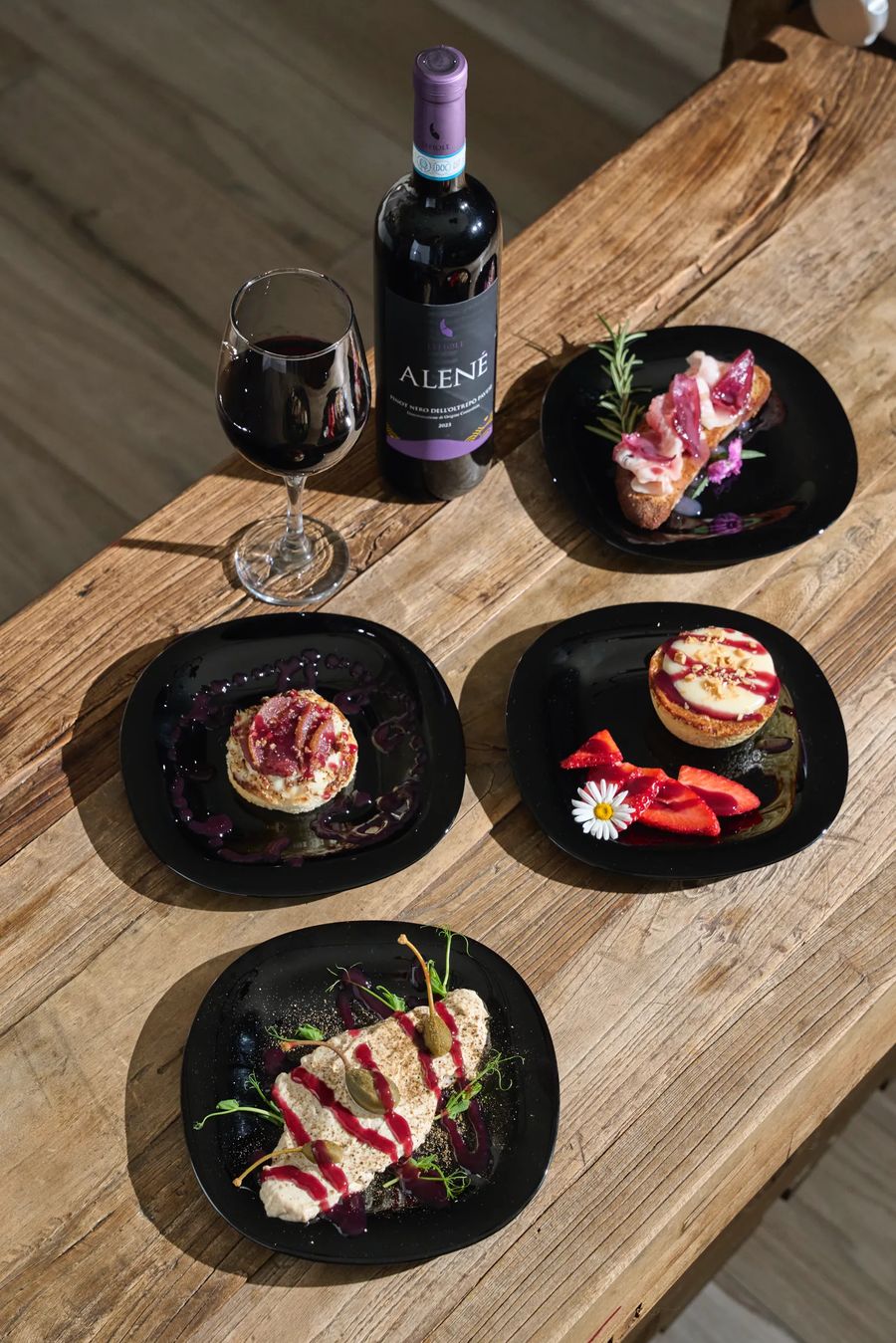 Selezione di antipasti su piatti neri: bruschetta con prosciutto, tartelletta con fragole e formaggio — fotografia menu ristorante Milano