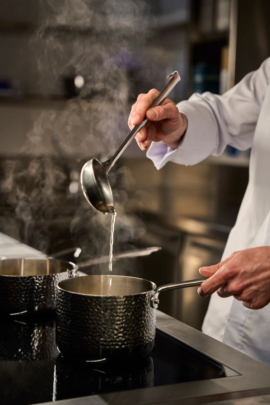 Chef che versa brodo fumante con mestolo su pentola in acciaio — backstage preparazione, fotografo reportage cucina ristorante Lombardia