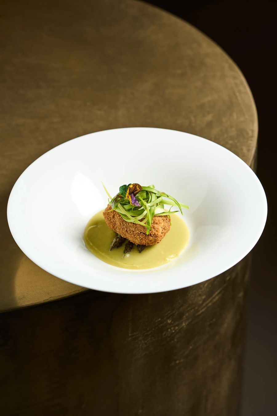 Crocchetta fritta su crema di asparagi con fiori eduli su piatto bianco e tavolo in bronzo — fotografo food stagionale ristorante Milano