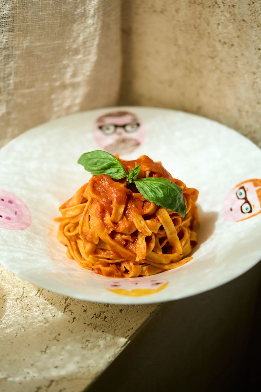 Tagliatelle al pomodoro fresco con basilico su piatto illustrato con ritratti — pasta italiana artigianale, fotografo ristorante FATA Milano
