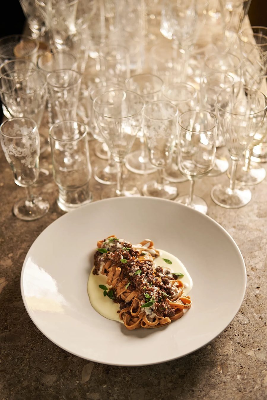 Tagliatelle al ragù con crema bianca su piatto fondo, sfondo di flute — fotografia pasta fresca ristorante Potafiori Milano
